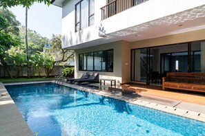 Uma casa moderna com piscina, um alpendre com banco de madeira e uma porta de vidro que dá para uma varanda.