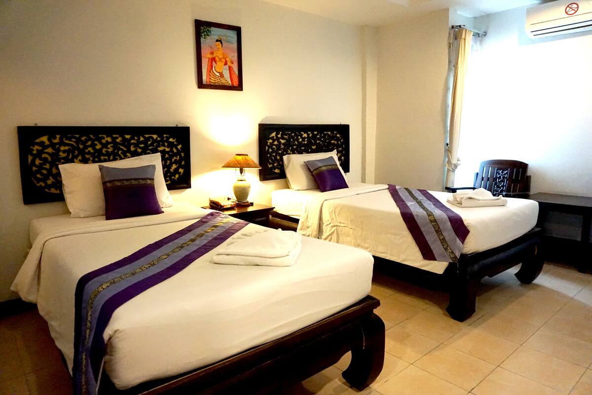 Een hotelkamer met twee bedden, elk met hoofdbord, een nachtkastje met lamp en een wandairconditioner.