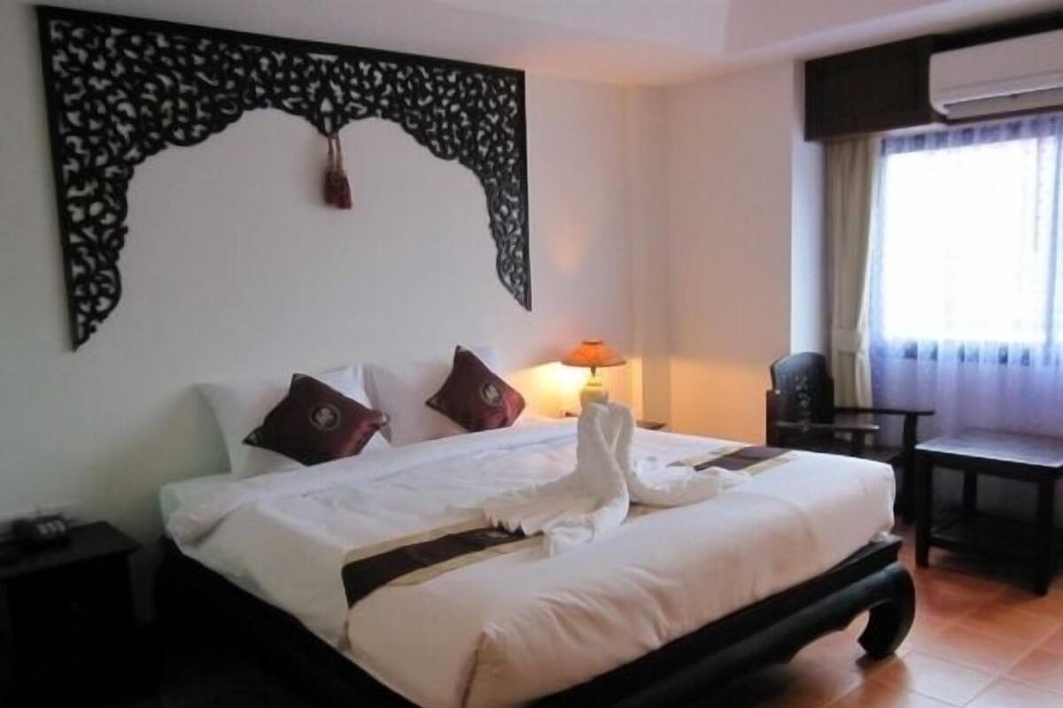 Een hotelkamer met een bed, nachtkastje, lamp, stoel en raam met gordijnen.
