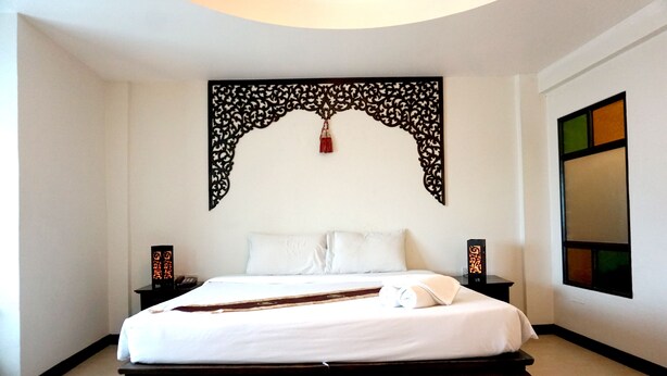 A neatly made bed with white linens, a decorative wall hanging above, and two bedside tables with lamps. - Wangburapa Grand Hotel (Chiang Mai)