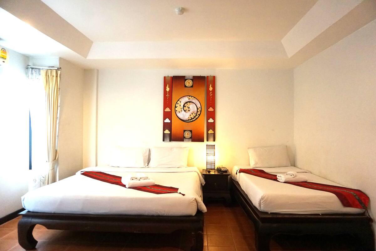 Een hotelkamer met twee bedden, een wandklok en een nachtkastje met een lamp.