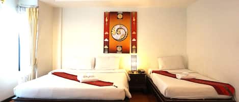Una camera d'albergo con due letti, una sveglia a muro e un comodino con una lampada.