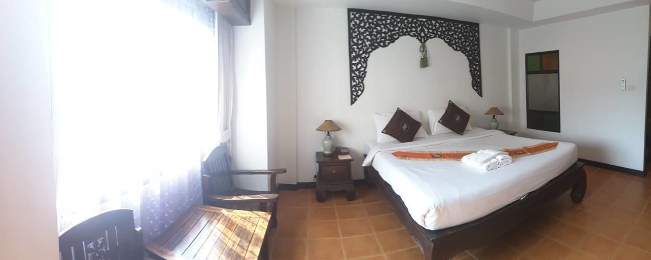 A hotel room with a bed, a desk, a chair, a nightstand with a lamp, and a decorative wall piece.