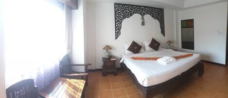 A hotel room with a bed, a desk, a chair, a nightstand with a lamp, and a decorative wall piece.