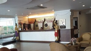 A reception area with a counter, decorative wall art, and wicker furniture. - Wangburapa Grand Hotel (Chiang Mai)