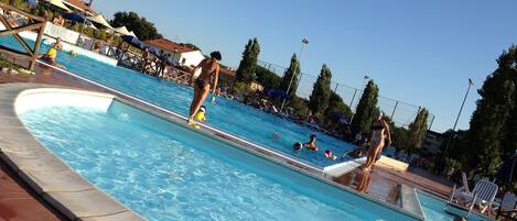 Una piscina al aire libre, sombrillas, sillones reclinables de piscina