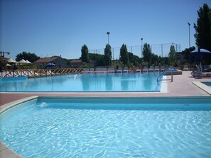 A swimming pool with clear water, surrounded by lounge chairs and umbrellas. - Villaggio Mare Si (Follonica)