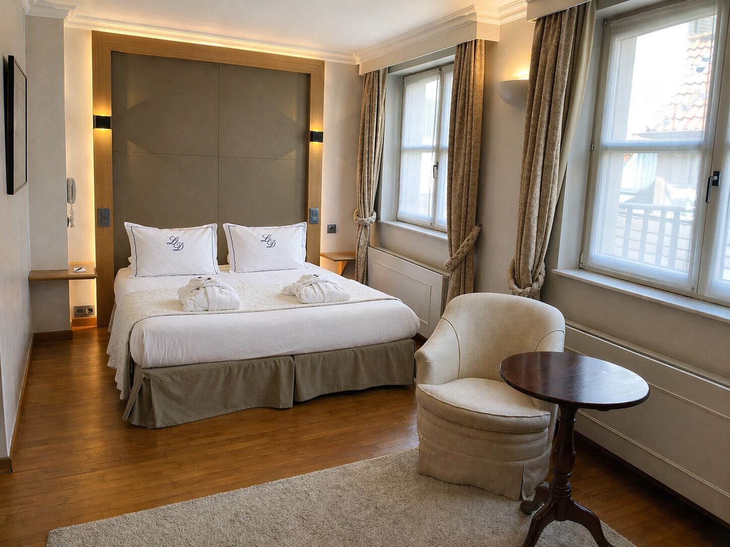 Habitación de hotel con una cama grande, una silla, una mesita y vistas al exterior por la ventana.