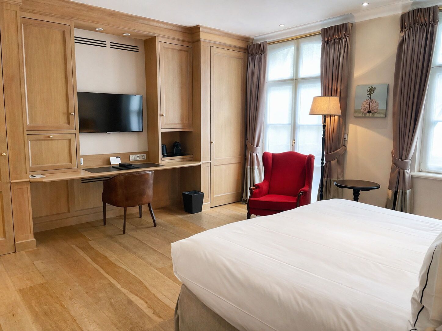 A hotel room with a bed, a desk with a chair, a television, a lamp, and a window with curtains.