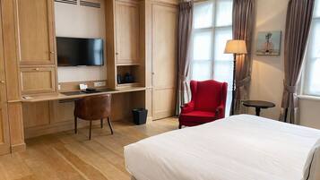 A hotel room with a bed, a desk with a chair, a television, a lamp, and a window with curtains.