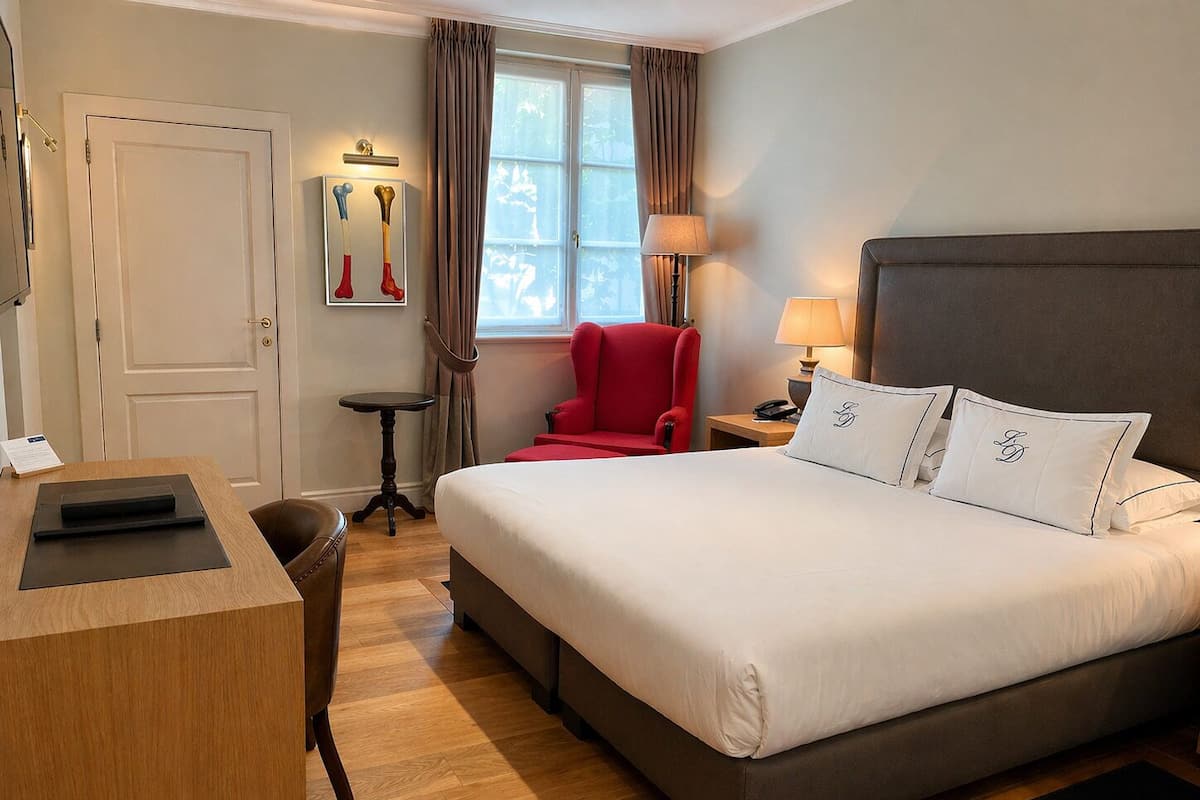 A hotel room with a bed, a desk, a chair, a lamp, and a window with curtains.