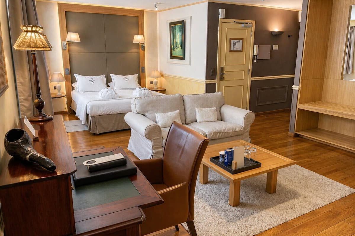 A hotel room with a bed, two sofas, a desk, and a coffee table.