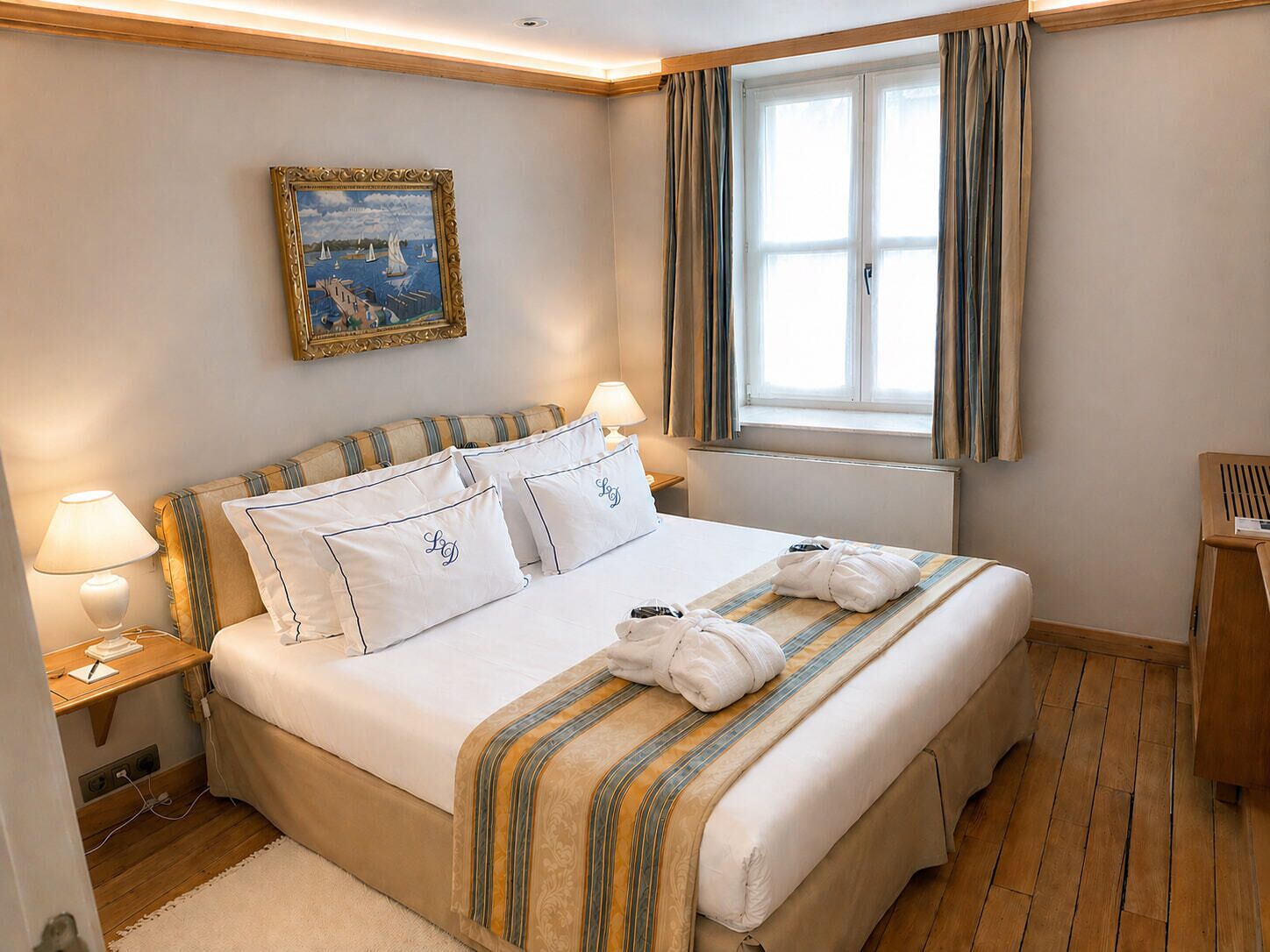 Habitación de hotel con cama, lámparas de noche, un cuadro, ventana con cortinas y suelo de madera.