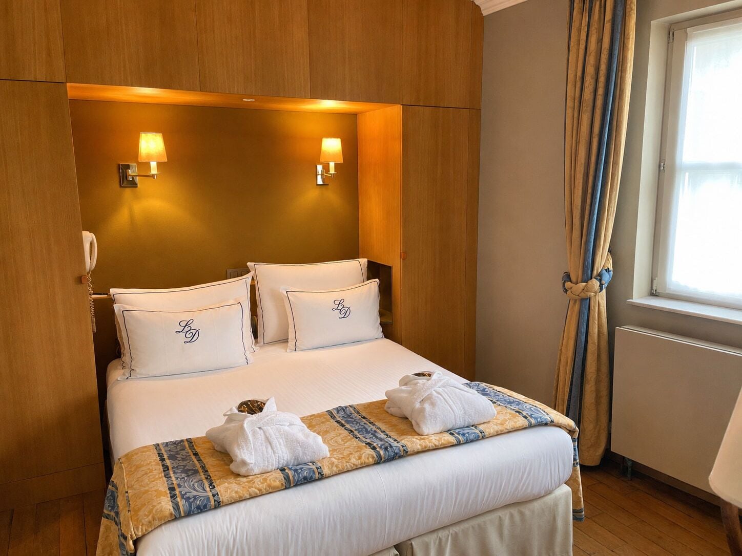 Ett hotellrum med en säng, två sänglampor, ett fönster med gardiner och en telefon.