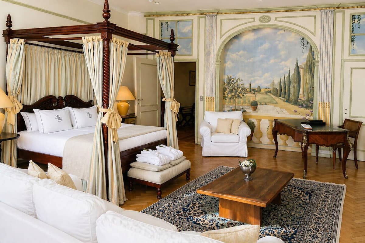 A four-poster bed with curtains, a white sofa, a wooden coffee table, and a large landscape painting on the wall.