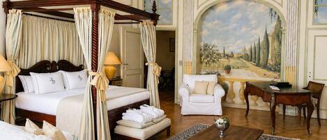 A four-poster bed with curtains, a white sofa, a wooden coffee table, and a large landscape painting on the wall.