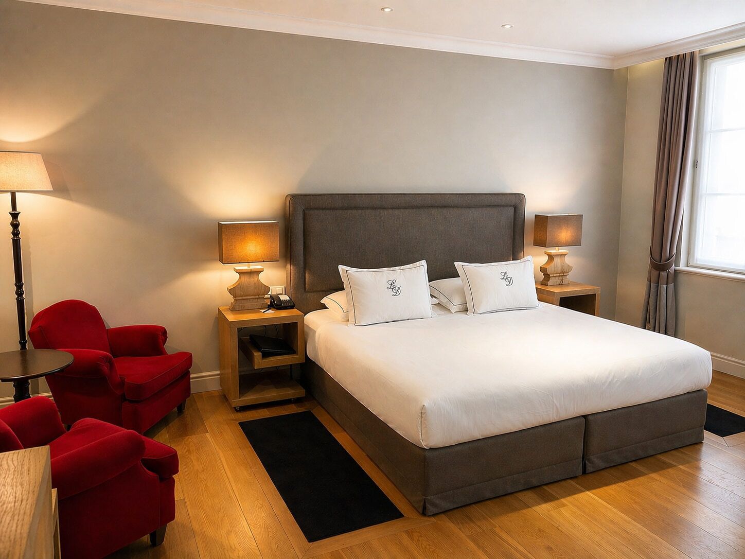 Een hotelkamer met een groot bed, twee nachtkastjes met lampen, een rode stoel en een houten vloer.