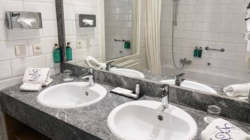 Un baño con dos lavamanos, una ducha, un perchero para toallas y un espejo.
