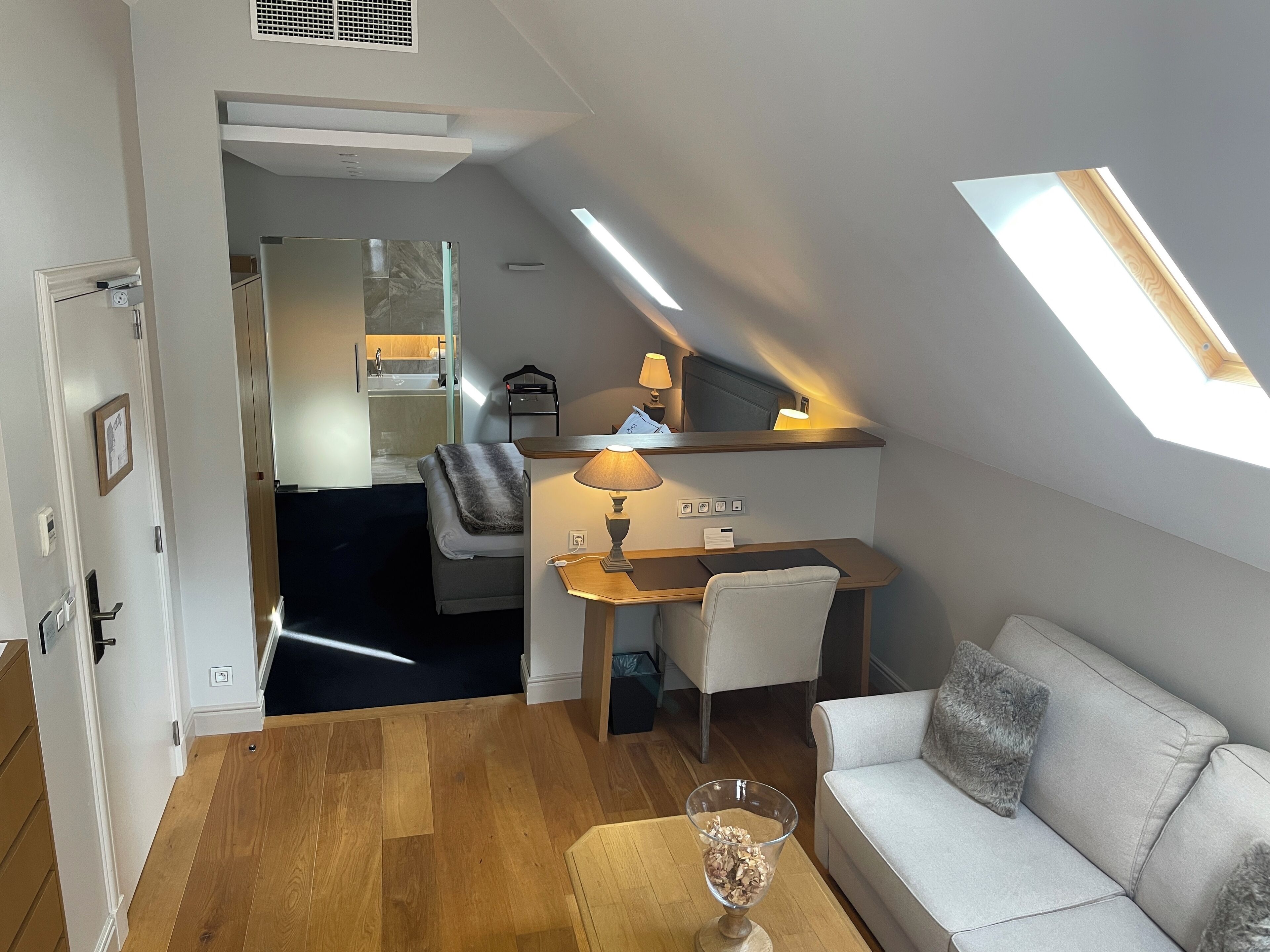 Een moderne loft slaapkamer met dakraam, een bureau met stoel, een bank en een glazen salontafel.
