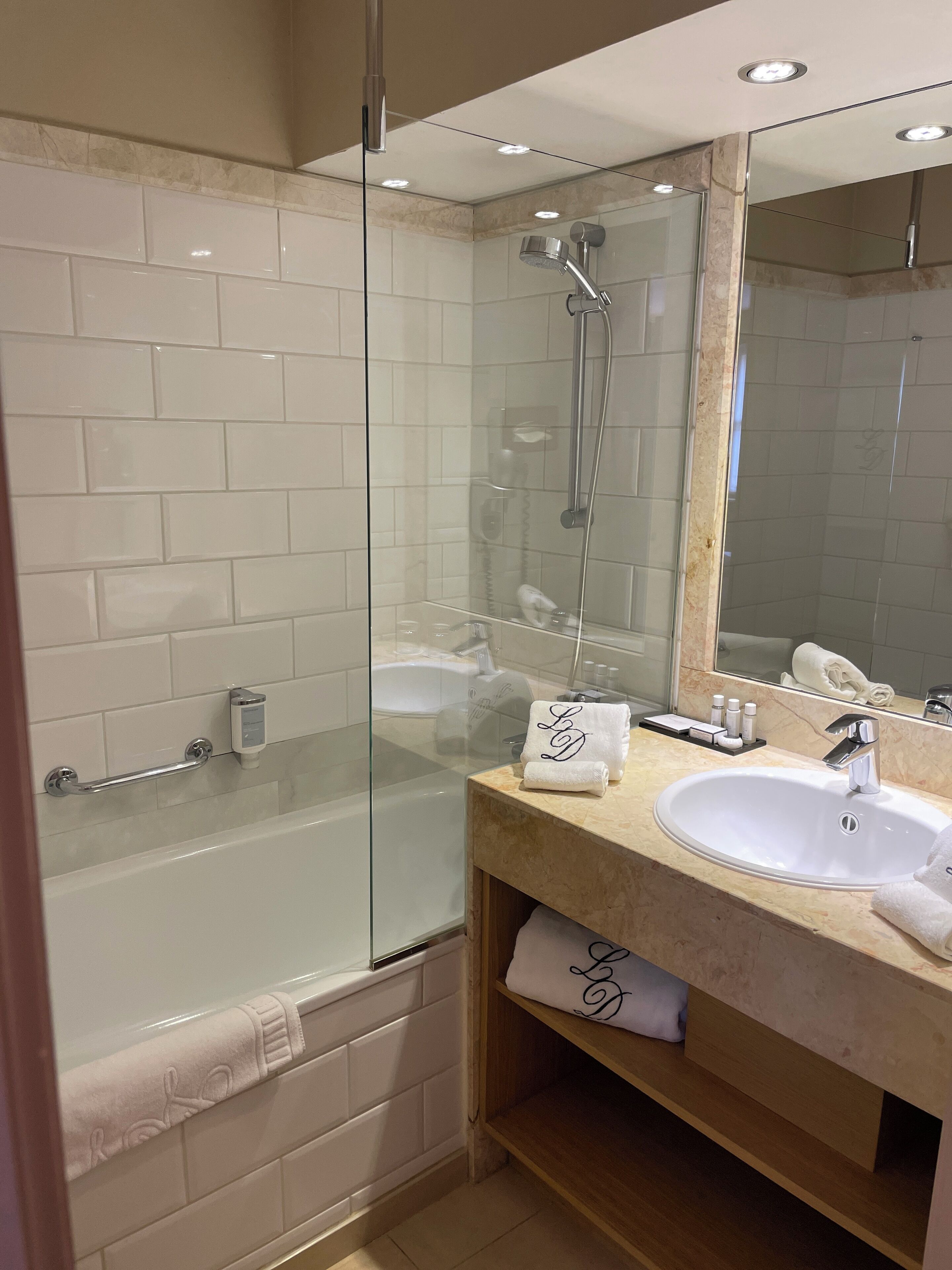 A modern bathroom with a glass-enclosed shower, a white bathtub, a vanity with a sink, and a large mirror.