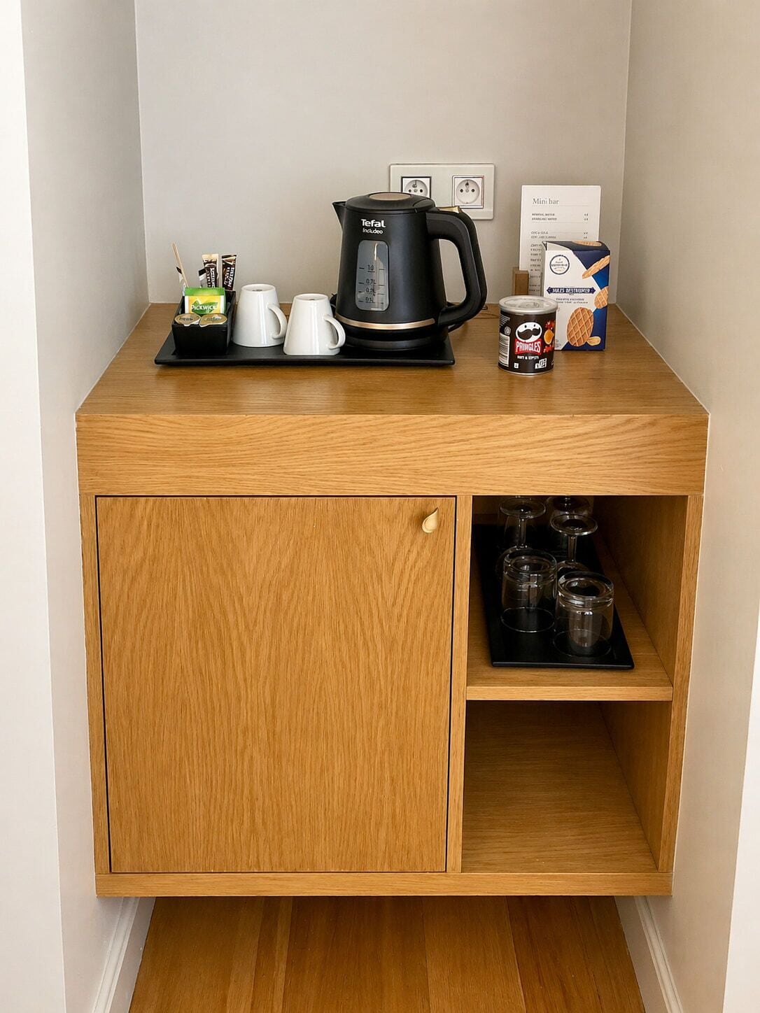 Una kitchenette de madera con una cafetera, tazas, una lata de Pringles y una caja de café instantáneo.