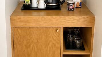Una kitchenette de madera con una cafetera, tazas, una lata de Pringles y una caja de café instantáneo.