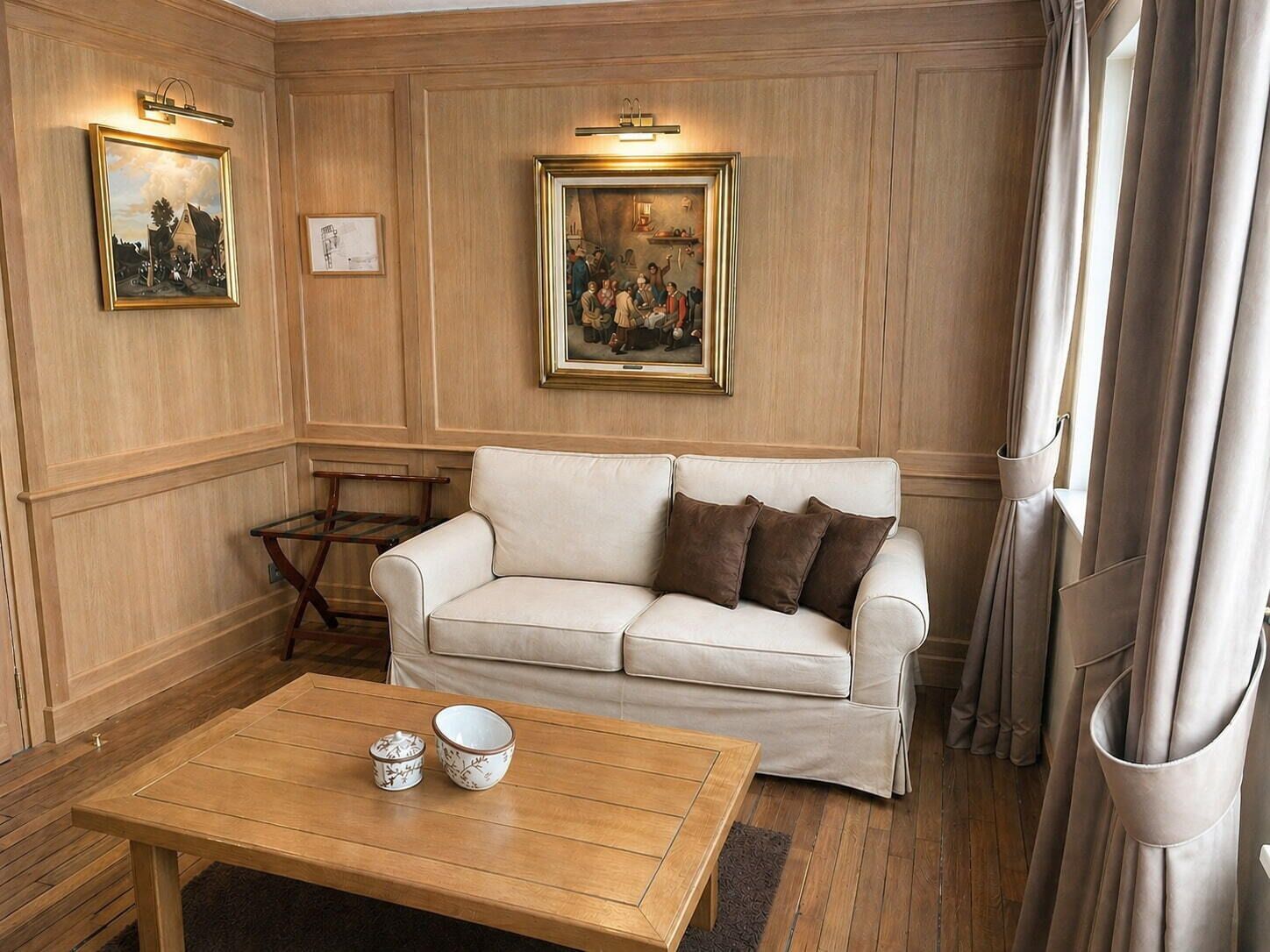 Une pièce avec un canapé beige, deux tableaux encadrés, une table basse en bois sur laquelle reposent deux bols, et une table d’appoint en bois.