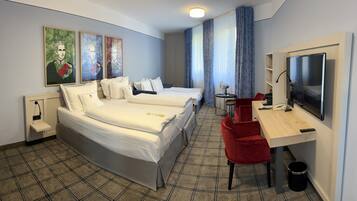 A hotel room with two beds, a desk with a TV, a chair, a small table with a lamp, and artwork on the wall.