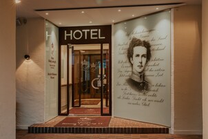 Entrada de un hotel con puerta de vidrio, un letrero que dice "HOTEL" y un felpudo de bienvenida.