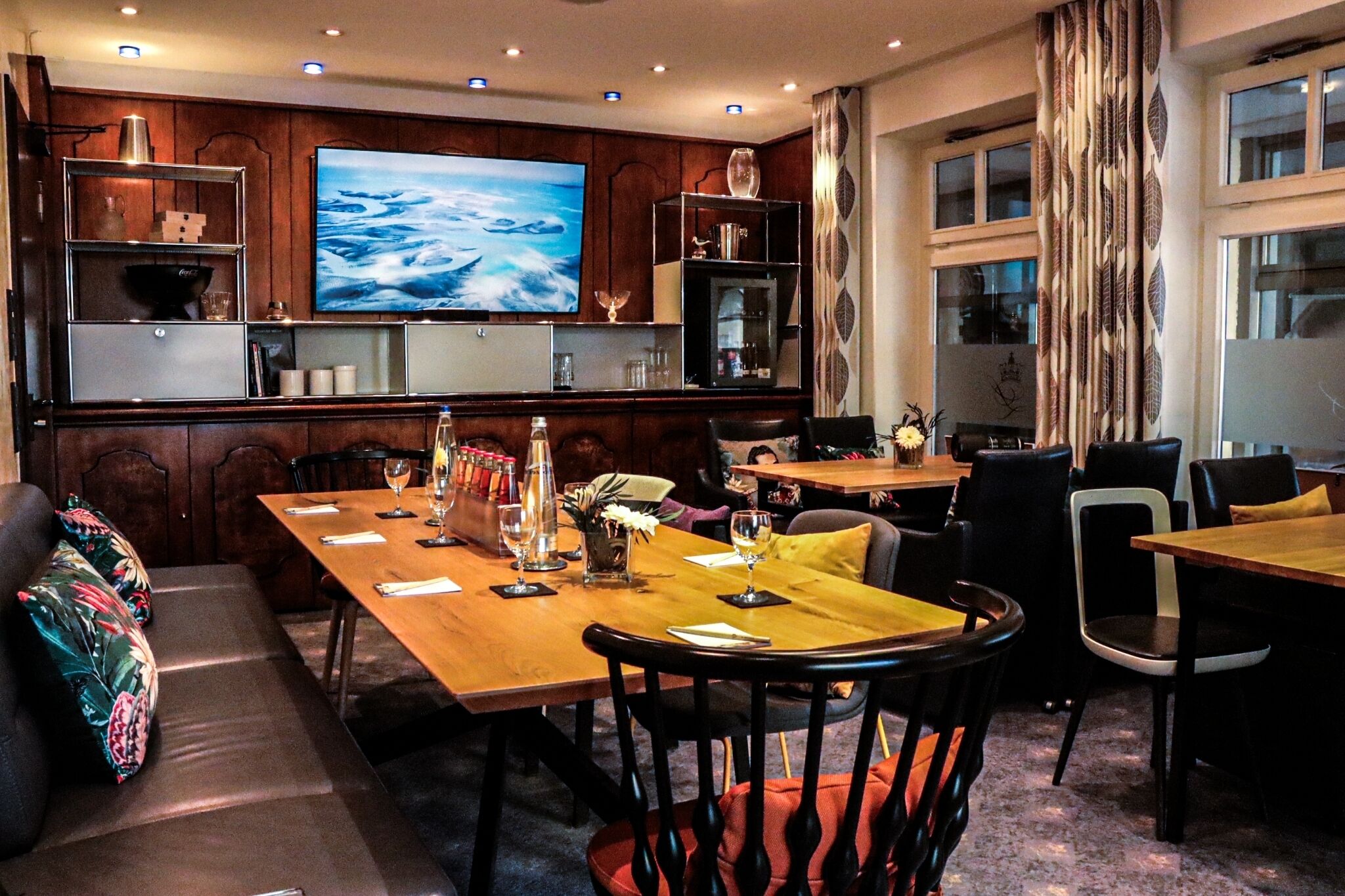 A dining area with wooden tables, chairs, and a large flat-screen TV mounted on the wall.