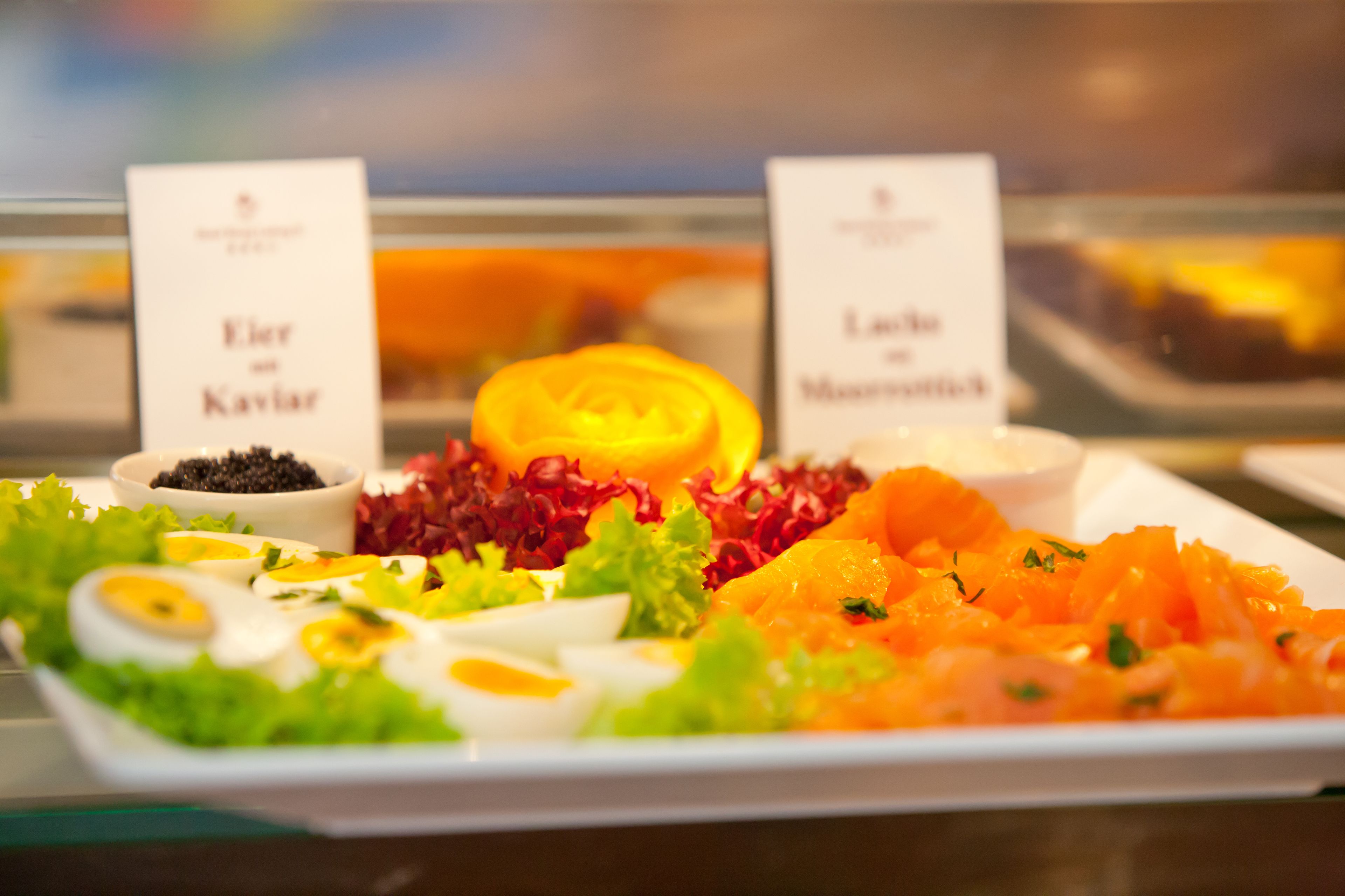Een buffet met borden met labels, waaronder 'Eier Kavlar' en 'Lachs Mohn'.