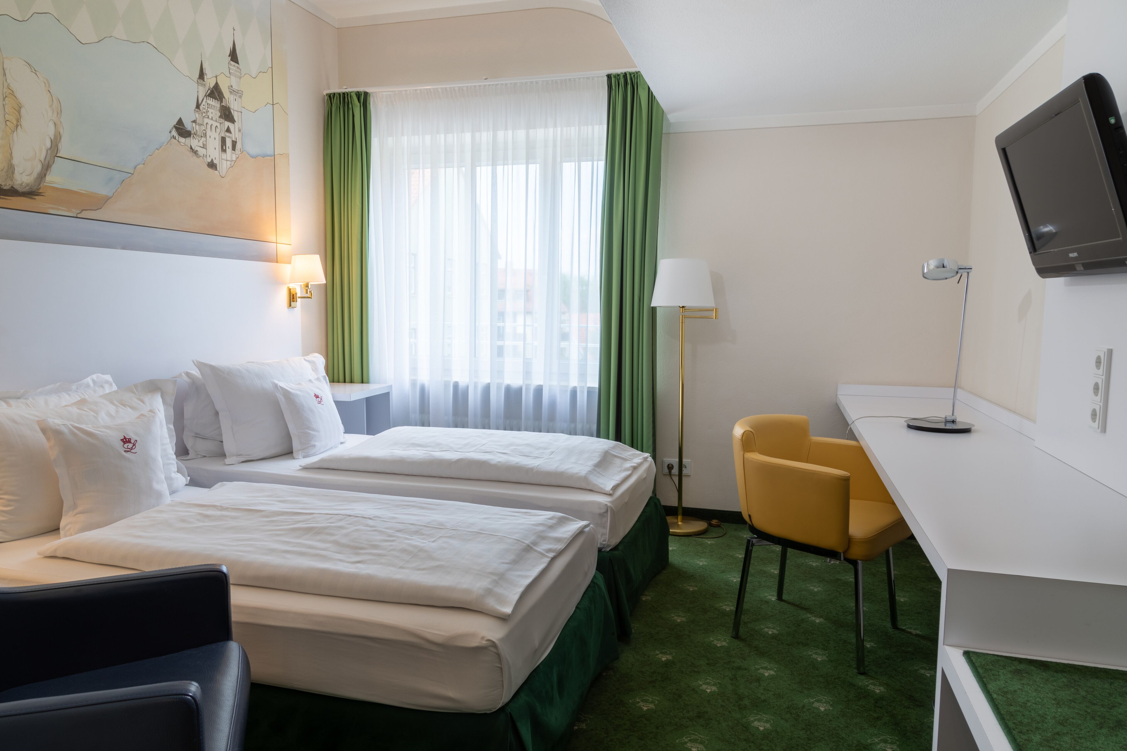 Habitación de hotel con dos camas, un escritorio, una silla, un televisor y una ventana con cortinas.