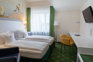 Habitación de hotel con dos camas, un escritorio, una silla, un televisor y una ventana con cortinas.