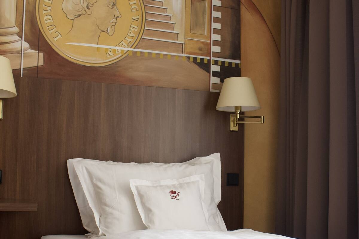 Una habitación de hotel con una cama bien hecha, un mural en la pared y una lámpara.