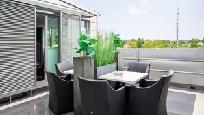 Un patio al aire libre con una mesa, sillas, una planta en maceta y vistas de la ciudad.