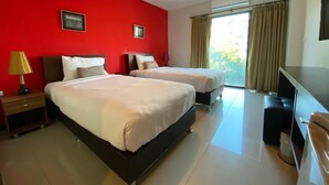 A hotel room with two beds, a desk, a lamp, and a large window with curtains. - WE Valley Hotel (Chiang Mai)