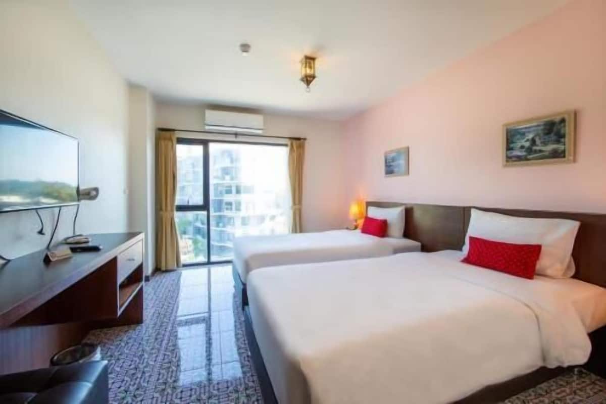 A hotel room with two beds, a desk, a television, and a window with a view.