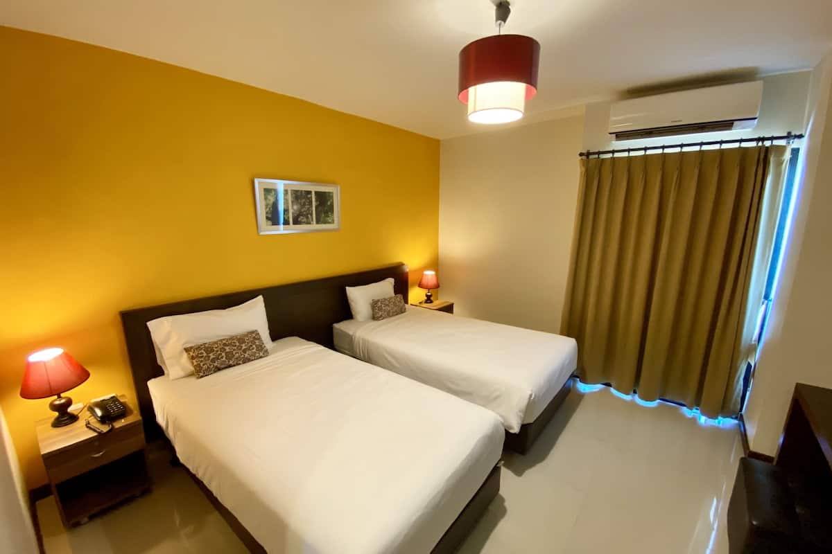 A hotel room with two beds, a nightstand with a lamp, a telephone, and a picture on the wall.