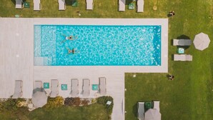 An aerial view of a swimming pool with two people swimming, surrounded by lounge chairs and umbrellas. - Hotel La Casa del Mulino (Merone)