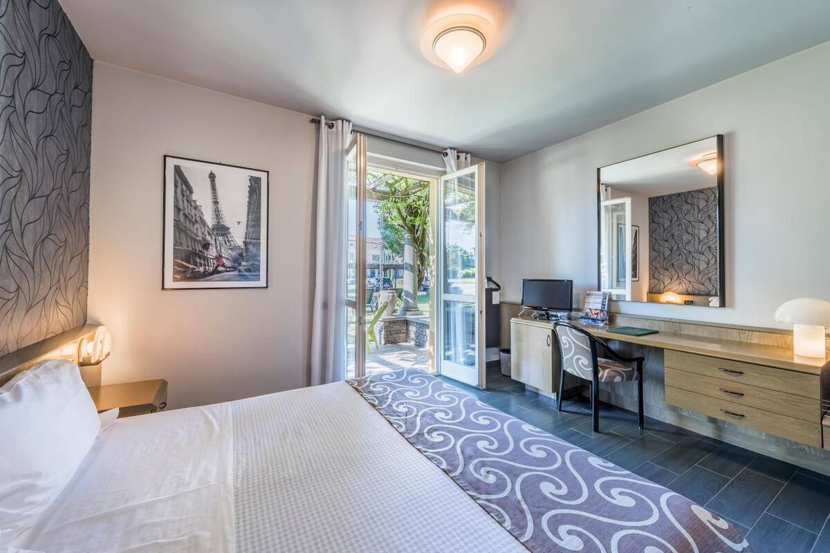 A hotel room with a bed, a desk, a chair, a television, and a large mirror.
