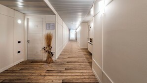 A hotel hallway with wooden flooring, white walls, and a door marked '103'. - Hotel La Casa del Mulino (Merone)