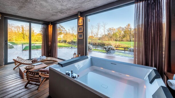 A modern spa area with a large bathtub, wooden deck seating, and a view of a golf course. - Hotel La Casa del Mulino (Merone)