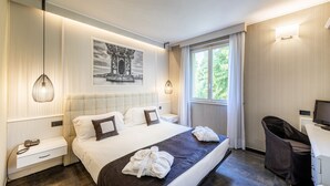 A hotel room with a large bed, a desk with a chair, a window with curtains, a painting on the wall, and a telephone on the nightstand. - Hotel La Casa del Mulino (Merone)