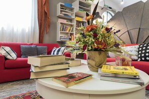 A living room with a red sofa, a coffee table with books and a vase of flowers, and a bookshelf in the background.