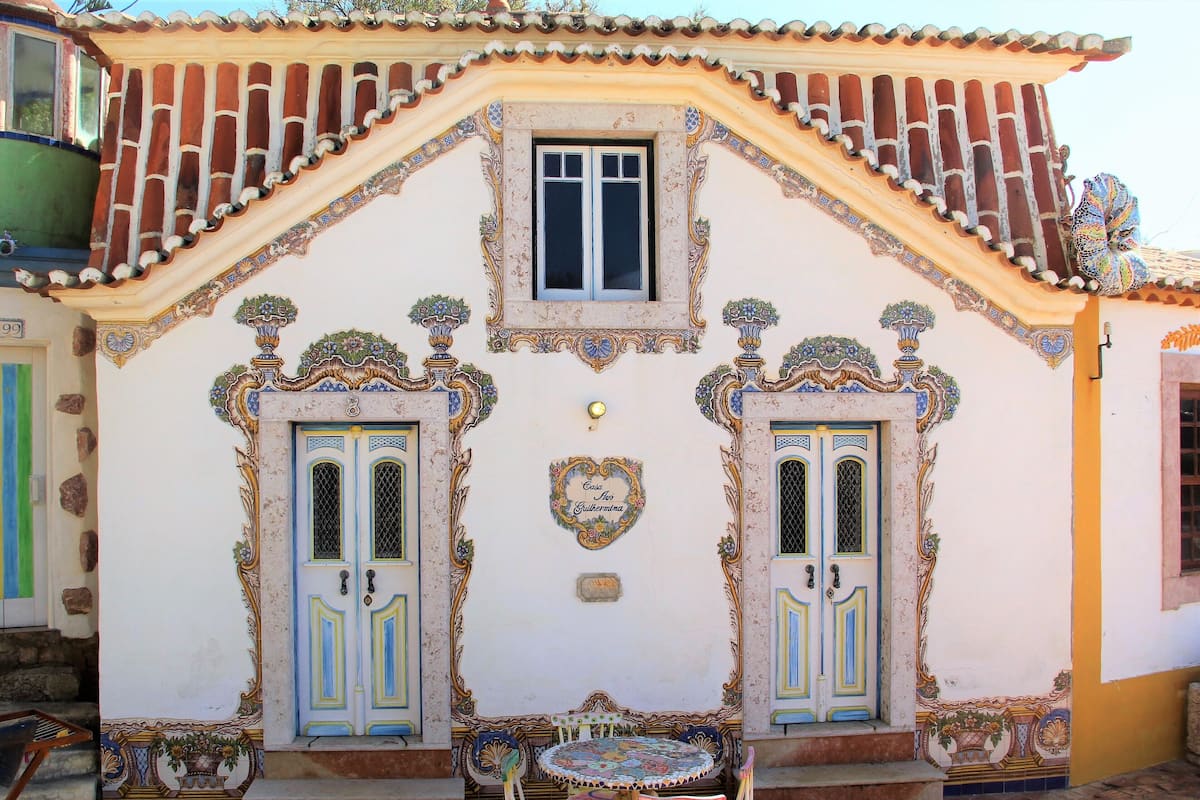 Ein Gebäude mit aufwendigen architektonischen Details, zwei symmetrischen Türen und einem kleinen Tisch mit Stühlen davor.