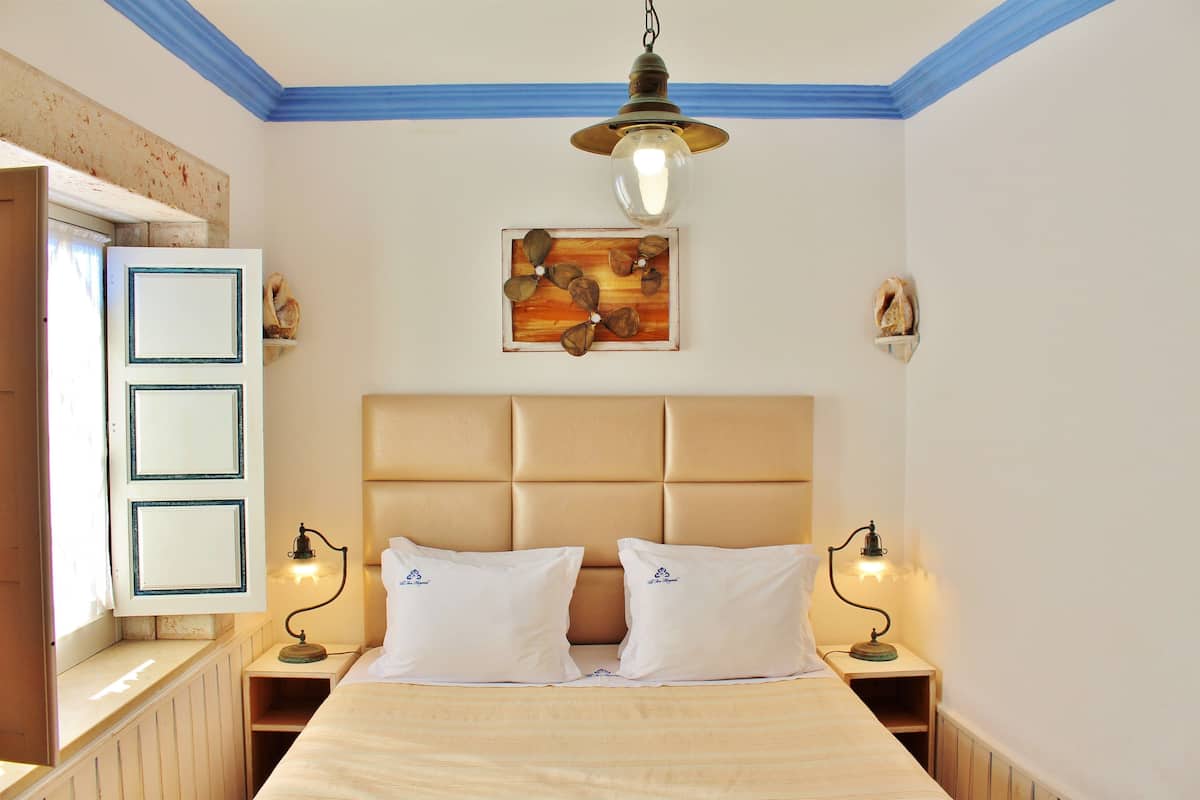 Ein Schlafzimmer mit einem großen Bett, zwei Nachttischen mit Lampen, einem Kopfteil, einem Bild an der Wand und einer Tür mit blauer Umrandung.