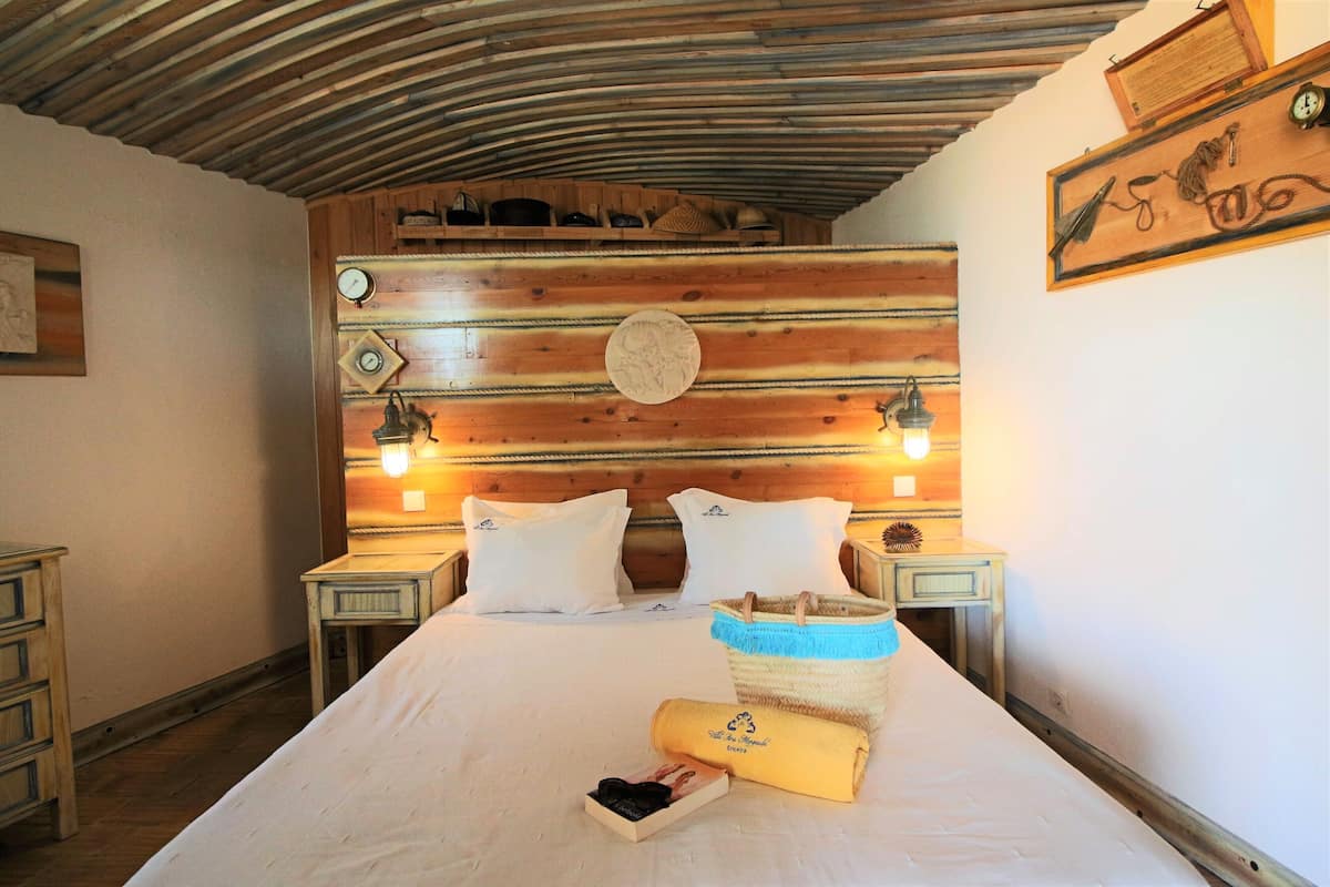 Ein Zimmer mit einem hölzernen Kopfende, zwei Nachttischen mit Lampen, einem Bett mit weißer Bettwäsche und einer Wanduhr.
