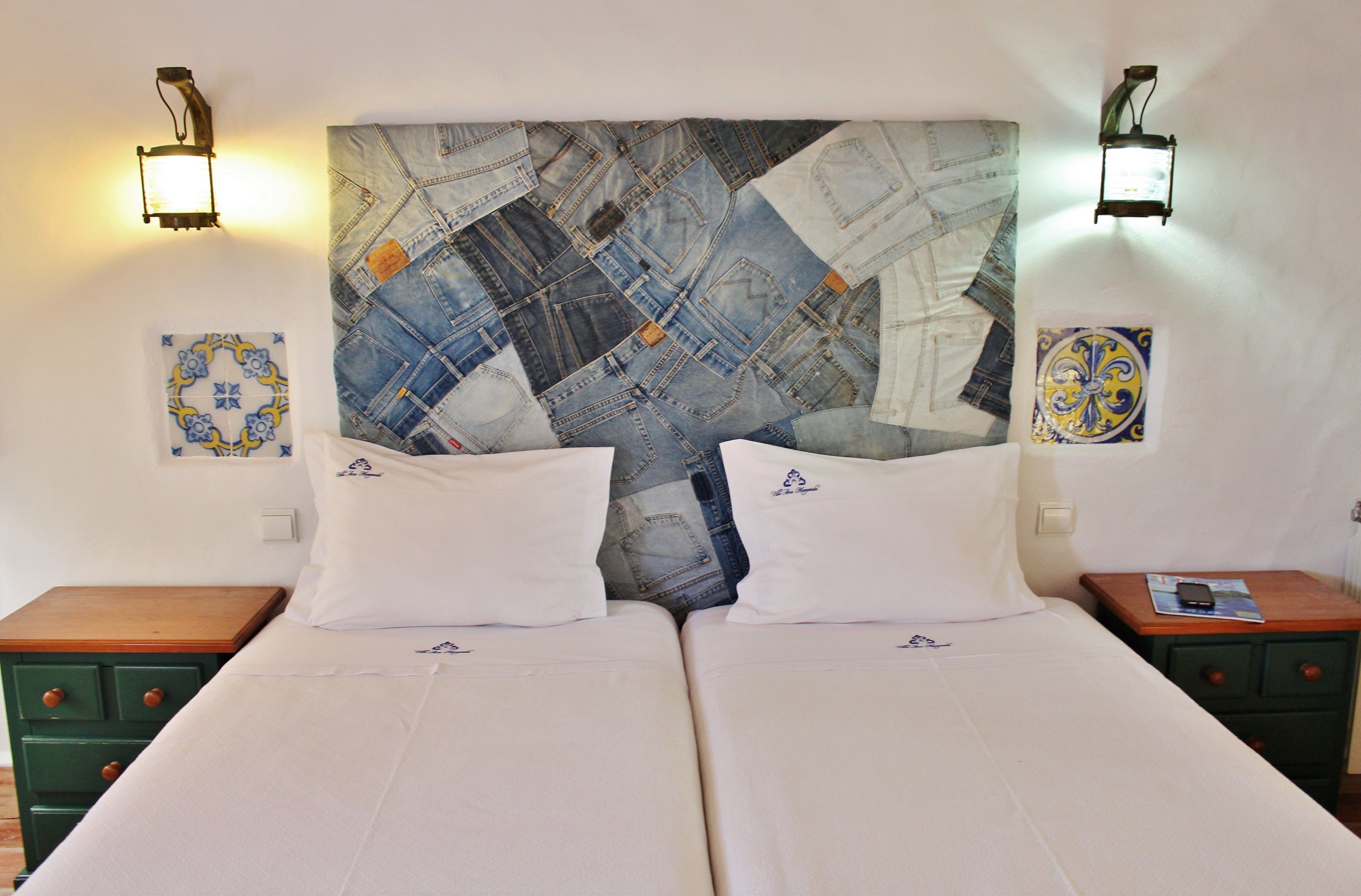 A double bed with white linens, two pillows, and a headboard with a denim patchwork design. There are two nightstands with wooden tops, one on each side of the bed.