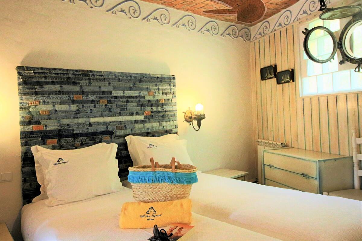 Ein Hotelzimmer mit einem Bett, das ein dunkelblaues Kopfteil hat, einem Nachttisch mit einer Lampe, einem kleinen Spiegel und einer hölzernen Kommode.