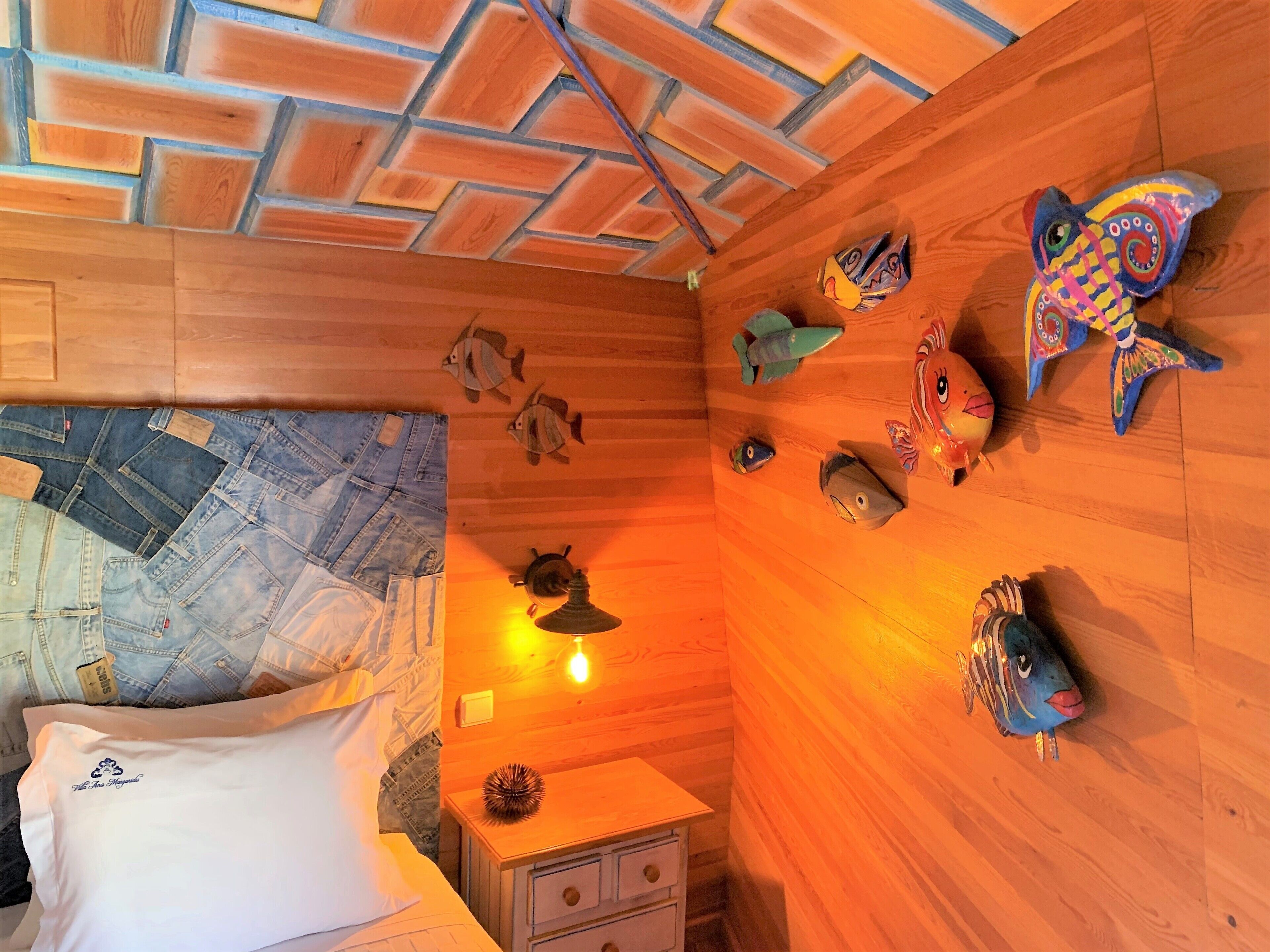 Ein Zimmer mit Holzwänden, einem Bett mit Jeansbezügen, einem Nachttisch und dekorativer Fischwandkunst.
